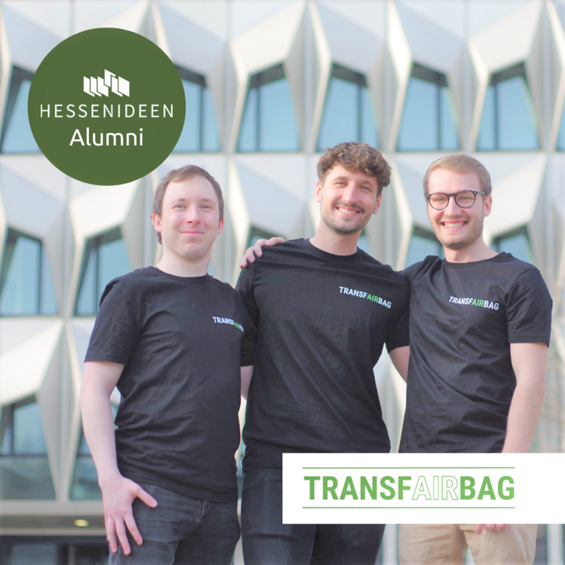 Auf dem Bild erkennt man drei junge Männer in den 20ern. Sie tragen schwarze Shirts mit der Aufschrift "Transfairbag" in weiß. Alle drei Männer haben dunkelblondes Haar. Der Mann links trägt eine beigefarbene Chino-Hose und eine Brille.